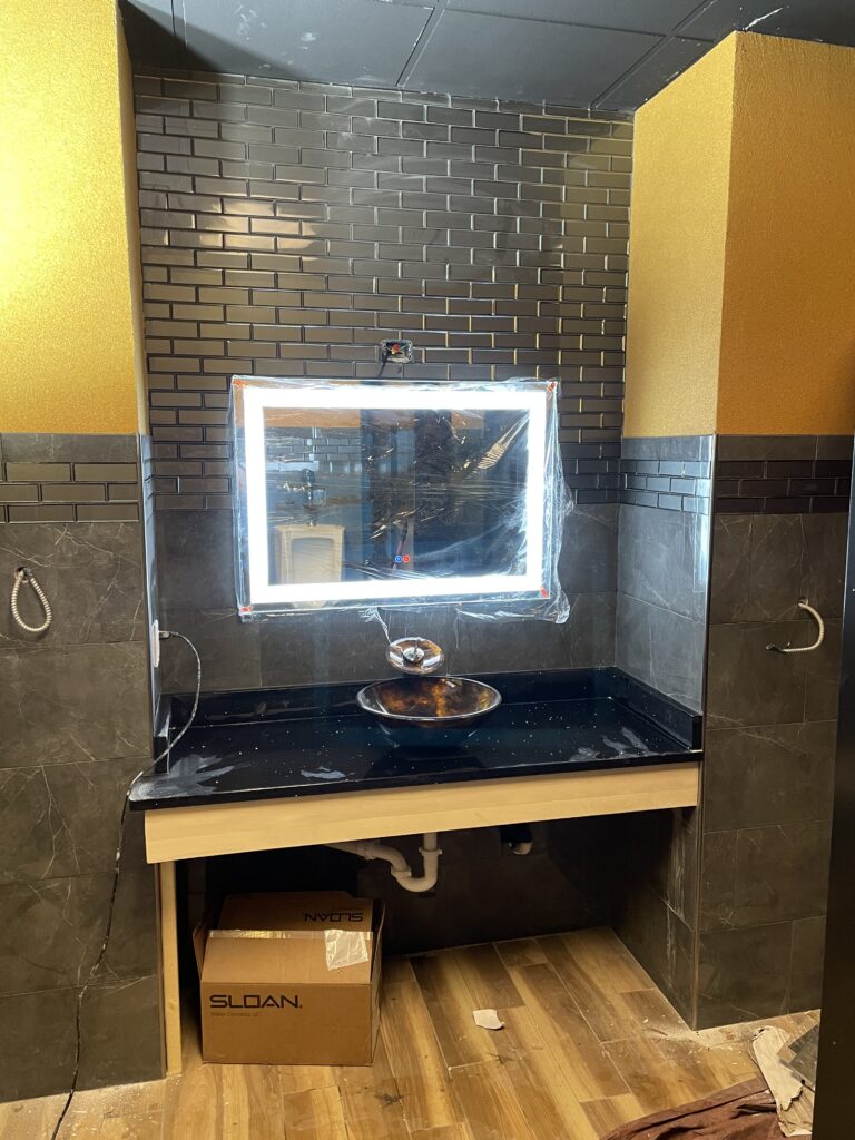 Bathroom sink area under construction with illuminated mirror.